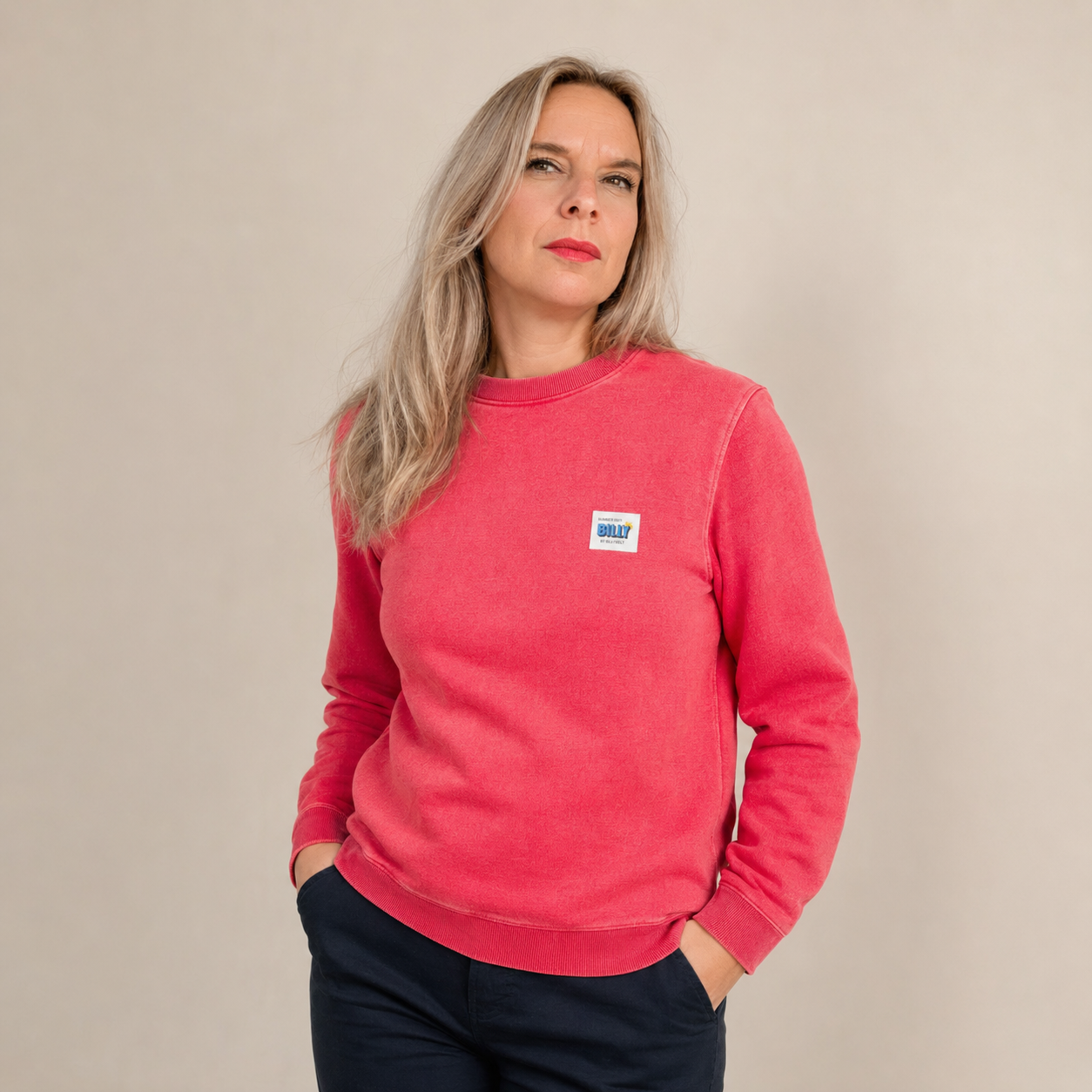 Jana trägt einen pink-roten Billybelt Pullover mit dezenter Waschung und kleinem Brustpatch vor einem neutralen Studiohintergrund.