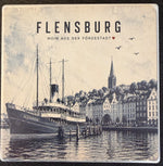 Bedruckte Fliese oder Untersetzer mit dem historischen Dampfschiff Alexandra vor dem Flensburger Hafen und dem Schriftzug „Flensburg – Moin aus der Fördestadt“ im Vintage-Design.
