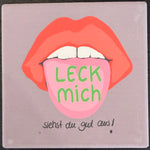 Bedruckte Fliese oder Untersetzer mit stilisierten roten Lippen und einer herausgestreckten Zunge mit der Aufschrift „Leck mich“, ergänzt durch den Spruch „Siehst du gut aus!“.