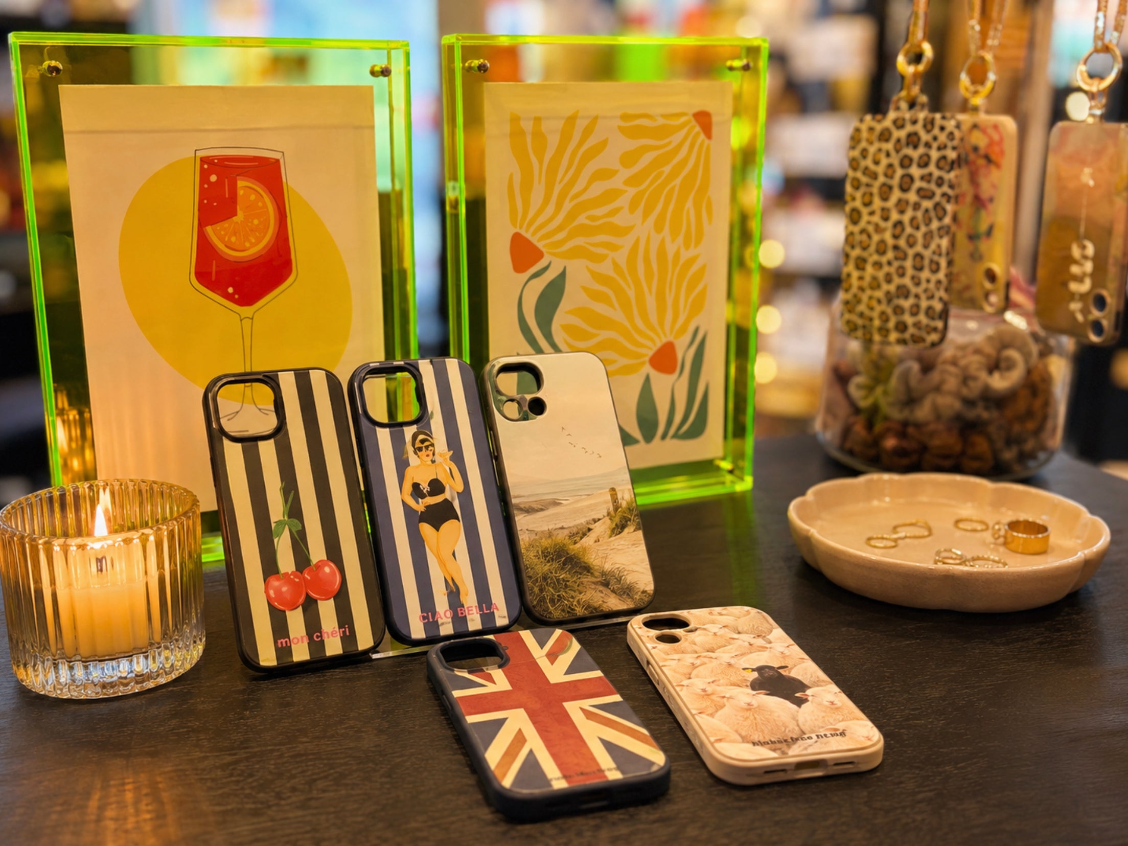 Beliebte Handyhüllen und Accessoires von Hübsches Ding, dekorativ im Laden zwischen leuchtenden Bilderrahmen und warmem Kerzenlicht präsentiert.