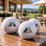 Drei weiße Golfbälle mit individuell gedrucktem geometrischem Firmenlogo auf einem Holztisch – Werbegeschenke von Hübsches Ding.