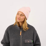 Model trägt eine pastellrosa Billybelt Wollmütze mit Logo-Patch zu einer dunkelgrauen Sherpa-Jacke