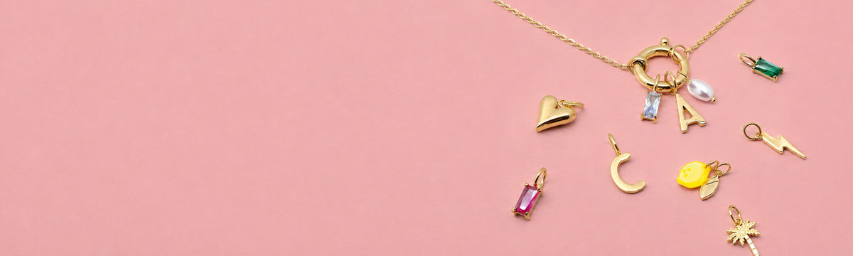 Little Jewellery Stories Kollektion mit goldener Halskette und farbigen Charms auf rosa Hintergrund