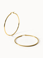 Goldene PURELEI Hoops Creolen mit 63 mm Durchmesser auf hellem Hintergrund